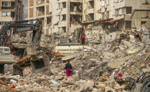 Un homme marche parmi les débris alors que des excavatrices démolissent les restes d’un bâtiment détruit suite au tremblement de terre à Samandag, dans le sud de la Turquie, le 22 février 2023. (Photo AP/Emrah Gurel)